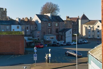 Urban scene: buildings surround a parking lot with cars, under bright sunlight, creating a calm, everyday atmosphere with visible textures and shadows in Caernarfon - Gwynedd - Wales - UK