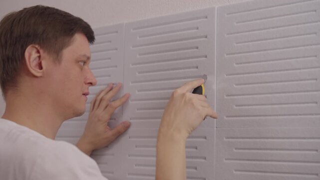 Professional handyman installing soundproof panel on wall using utility knife in home renovation project, performing soundproofing work for noise reduction and room acoustics improvement, slow motion.