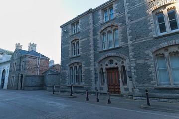 Gray stone building with arched windows and wooden door faces the viewer, adjacent brick structure, under bright, diffused light, creating a somber, architectural scene in Caernarfon - Gwynedd - Wales