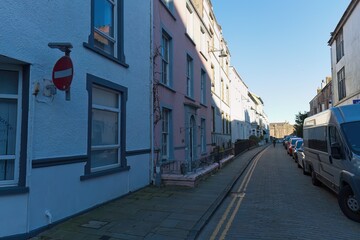Narrow street lined with pastel-colored buildings, bright sunlight, no entry sign, parked vans, creating a quaint, peaceful, and slightly compressed perspective in Caernarfon - Gwynedd - Wales - UK