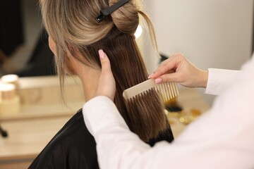 Hairdresser combing woman's hair in salon, closeup