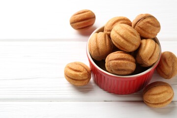 Delicious nut shaped cookies with boiled condensed milk in bowl on white wooden table, closeup. Space for text