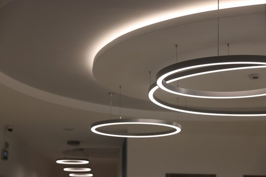 Stylish illuminated lamps on white ceiling indoors, closeup