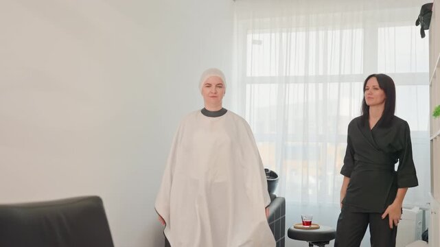 stylist and client in salon consultation preparing head cap under soft lighting professional adjusts cape and equipment, modern white studio, calm focused atmosphere, mutual conversation