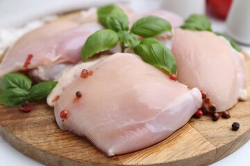 Raw chicken thighs with basil and peppercorns on white table, closeup