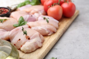 Raw chicken thighs with herbs, peppercorns and tomatoes on light table, closeup