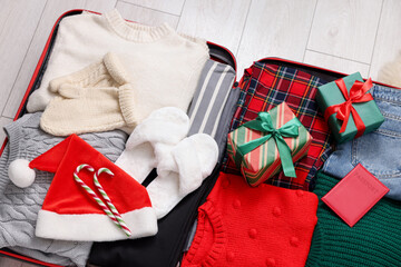 Christmas vacation. Suitcase with Santa hat, clothes, candy canes and gift boxes on floor indoors, top view