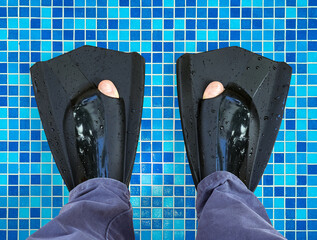 Wet black swimming flippers on feet standing on tiled surface of swimming pool. Close-up of diving equipment after water activity © Pihuliak