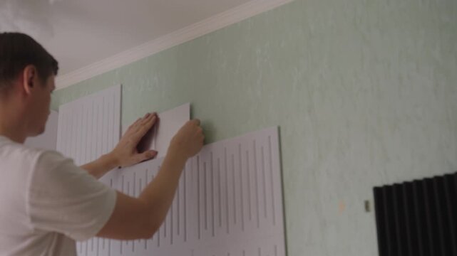 Man applying decorative mirror panels to textured wall, creating new focal point and modern aesthetic in home improvement project through careful diy installation. Shooting in slow motion.