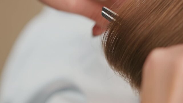 closeup stylist trimming blunt hair ends fine comb holding section, delicate shears snipping micro lengths, light brown strands falling, focused hands with steady motion, salon cape visible, calm