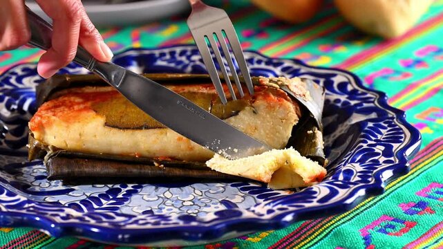 Close-up of cutlery cutting a hot tamale wrapped in a banana leaf. Mexican food