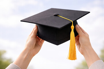 Graduation cap with yellow tassel held by hands against blurred outdoor background, symbolizing academic achievement and celebration of success