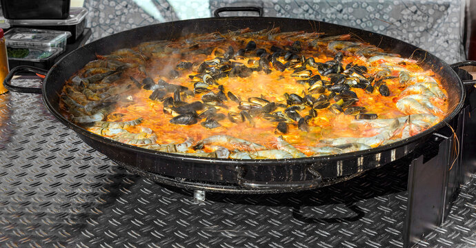 giant paella pan brimming with rice, mussels, shrimp, and vegetables simmers over an open flame, creating a delicious aroma