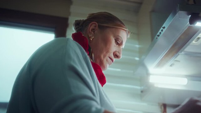 Low angle close-up of a focused woman cooking at home under a kitchen extractor hood with warm light and steam.
