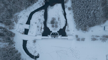 Aerial winter river with dam and island in Belarus, conifers line banks
