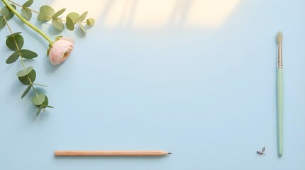 Clean flat lay of a blue workspace with a single pink ranunculus flower, eucalyptus, and a pencil.