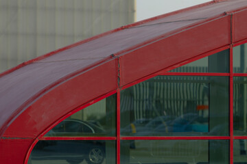 red curved metal canopy over glass showing weathered seams and subtle paint wear, parked car reflections visible in tinted panes,