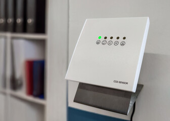 CO2 sensor indicating healthy office air quality. Carbon dioxide monitor with green indicator light mounted on office wall, showing good indoor air quality in modern workplace.