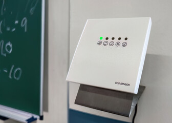 CO2 sensor showing good indoor air quality in classroom. Wall-mounted carbon dioxide monitor with green indicator light in a classroom, showing good indoor air quality and healthy learning environment