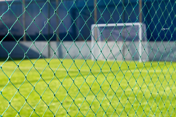 Green fence mesh on a sunny sports field with soccer goals