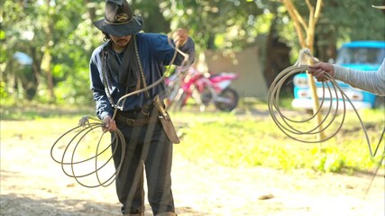 A cowboy handling a lasso rope for training at a rustic camp setup with wooden storage and cooking tools in the background