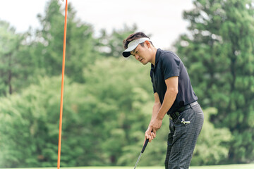 Male golfer (putter) playing golf on the green of a golf course