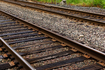 Transportation Infrastructure: Close-Up of Railway Tracks with Wooden Sleepers and Gravel Ballast Lined by Greenery in Rural Setting