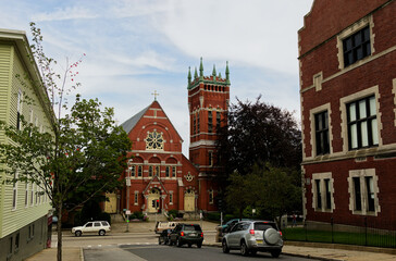 Fototapeta premium Historic Urban Architecture: Red Brick Church and Tower Amidst City Street with Cars and Trees, Vertical Composition