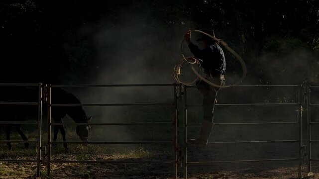 A cowboy training a horse in a dusty corral at sunrise, creating a dramatic western silhouette