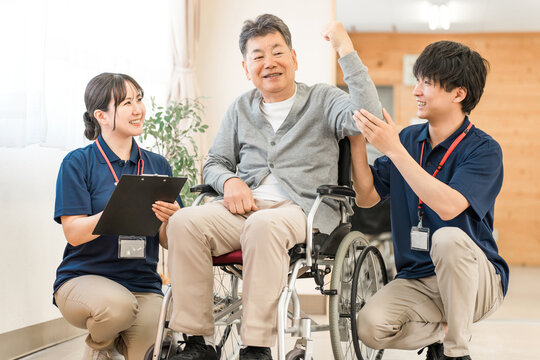 Senior/elderly man doing chair exercises, exercise and rehabilitation at a nursing facility, with physiotherapist, caregiver and trainer