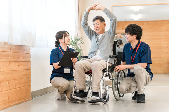 Senior/elderly man doing chair exercises, exercise and rehabilitation at a nursing facility, with physiotherapist, caregiver and trainer