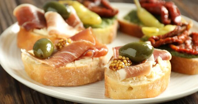 Tasty bruschettas with prosciutto and sun-dried tomatoes spinning on wooden table, closeup