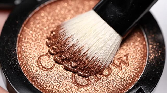 Close-up of a makeup brush applying shimmering bronzer in a compact