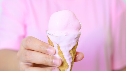 Young woman wearing pink shirt, holding melting strawberry ice cream cone, enjoying sweet summer moment with creamy dripping dessert