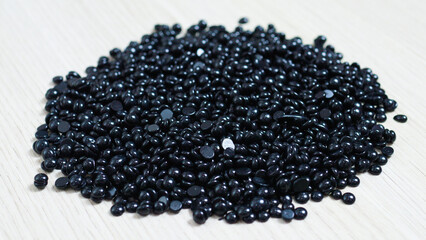 Dark depilation wax beans scattered on pale wooden surface, highlighting texture contrast between deep black pellets and smooth light background