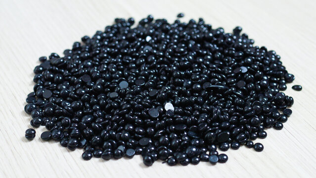Dark depilation wax beans scattered on pale wooden surface, highlighting texture contrast between deep black pellets and smooth light background