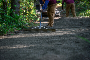 Obraz premium Landscaping maintenance crew using rakes and spreading freshly laid gravel on a woodland trail in a forest park 