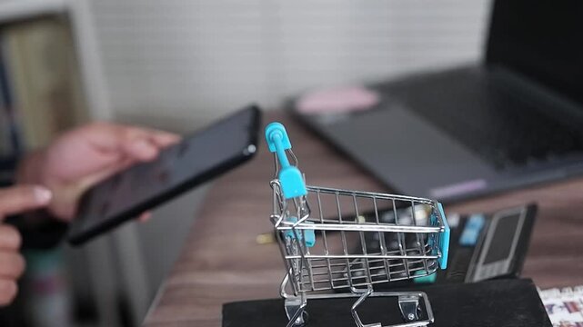 Concept of online shopping, clothing selection and online payment. Man's hand and mobile phone screen with fashion e-commerce for shoe selection, purchase and sale. small shopping cart on table.
