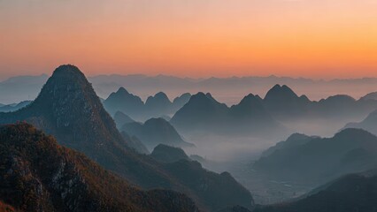 Misty mountain range with peaks at sunrise orange sky layered landscape