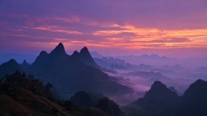 Obraz premium Mountain peaks shrouded in mist during a vibrant purple and orange dawn sky