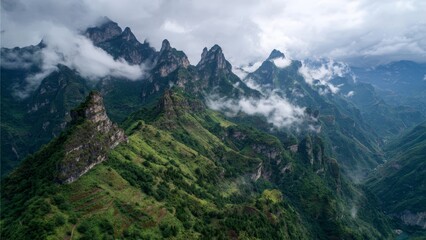 Jagged green mountain peaks emerge from atmospheric clouds in a misty rugged landscape