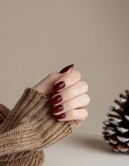 Elegant Hand Displaying Deep Red Manicure with Knitted Sweater and Pinecone Accent