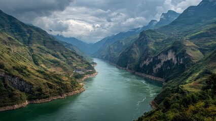 Obraz premium A wide deep river flows between steep green terraced mountains under a cloudy sky