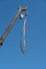 Crane lift with metal beam against clear blue sky during daytime work site operations