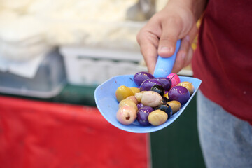A person holds a scoop filled with colorful olives at a market
