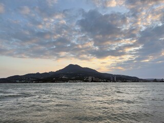 Fototapeta premium Tamsui Cityscape with Mountain Backdrop: A breathtaking view of the urban waterfront in Taiwan during a rich orange sunset featuring the dramatic silhouette of the dynamic mountain landscape.