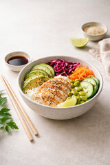 A vibrant poke bowl with grilled chicken, fresh vegetables, and rice, served with chopsticks and soy sauce.