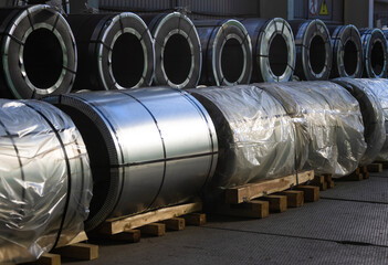 Steel coils wrapped in plastic sit on wooden pallets in a warehouse. The setting shows organized storage in an industrial space during daylight.