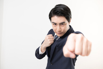 パンチやガッツポーズで気合いを入れるスーツのビジネスマン男性の勝利や成功、チャレンジのファイティングポーズ　白背景のカメラ目線