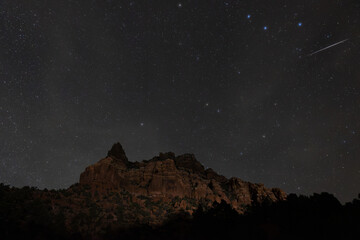 A bright meteor streaks through the upper right corner of the frame above an unnamed peak jutting up into the sky above the Smith Mesa road in Southern Utah USA during the Orionid meteor shower in Dec
